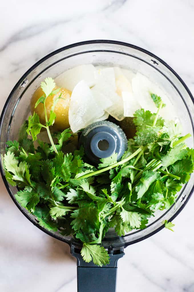 Food processor filled with all the ingredients needed to make salsa verde.