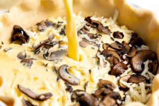 Pouring egg mixture on top of mushrooms in pie dish.