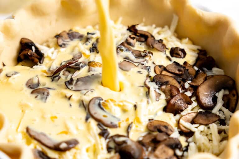 Pouring egg mixture on top of mushrooms in pie dish.