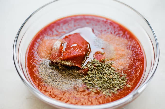 Bowl filled with tomato sauce, paste, olive oil and seasoning. 