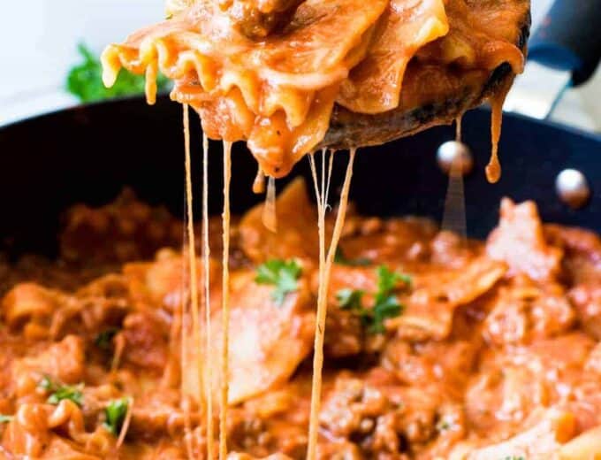 Wooden spoon scooping up lasagna pasta with strings of cheese coming back down to the skillet.