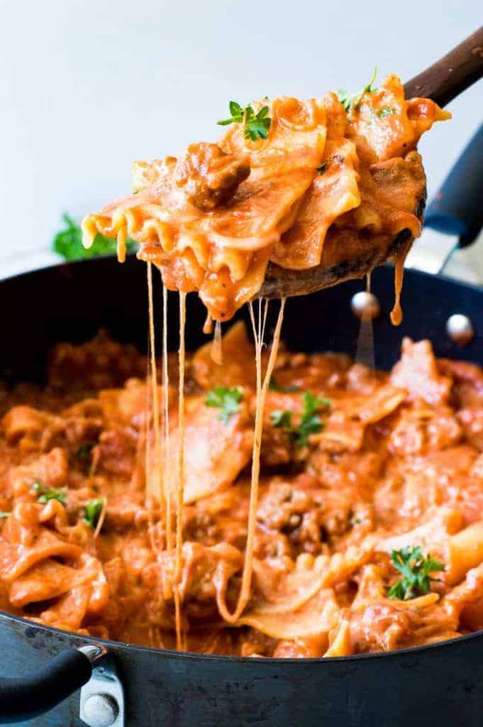 Wooden spoon serving up lasagna skillet pasta with strings of cheese coming down. 