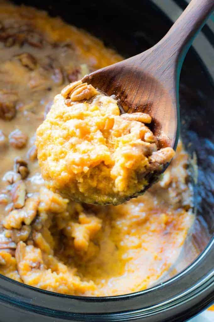 Wooden Spoon scooping up sweet potato casserole with a sweet brown sugar pecan topping.