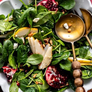 Salad with pomegranate, pear, pecans, and goat cheese with a wooden handled serving spoon.