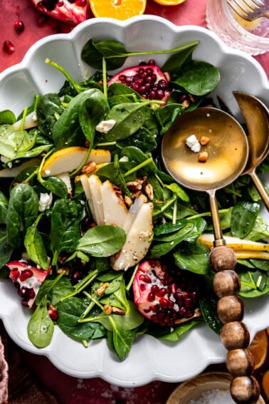 Salad with pomegranate, pear, pecans, and goat cheese with a wooden handled serving spoon.