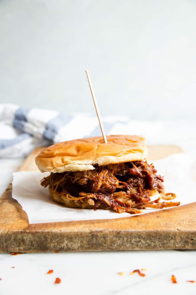 Pulled pork sandwich made with slow cooker pulled pork on a wooden cutting board.