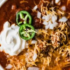 Bowl full of Texas Chili. Topped with cheese, sour cream, white onion and jalapeno.