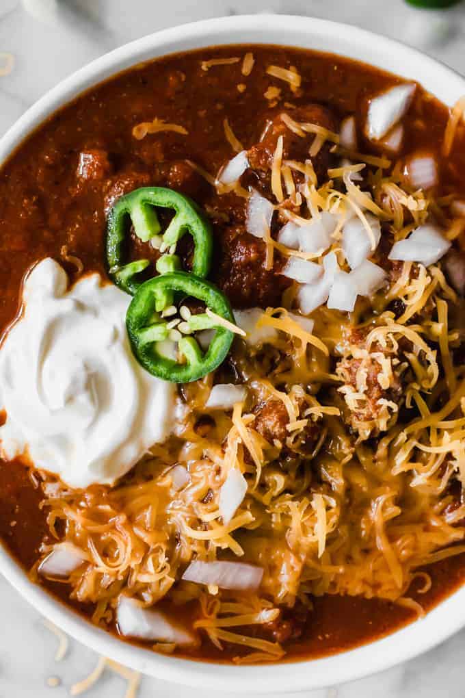 Bowl full of Texas Chili. Topped with cheese, sour cream, white onion and jalapeno.