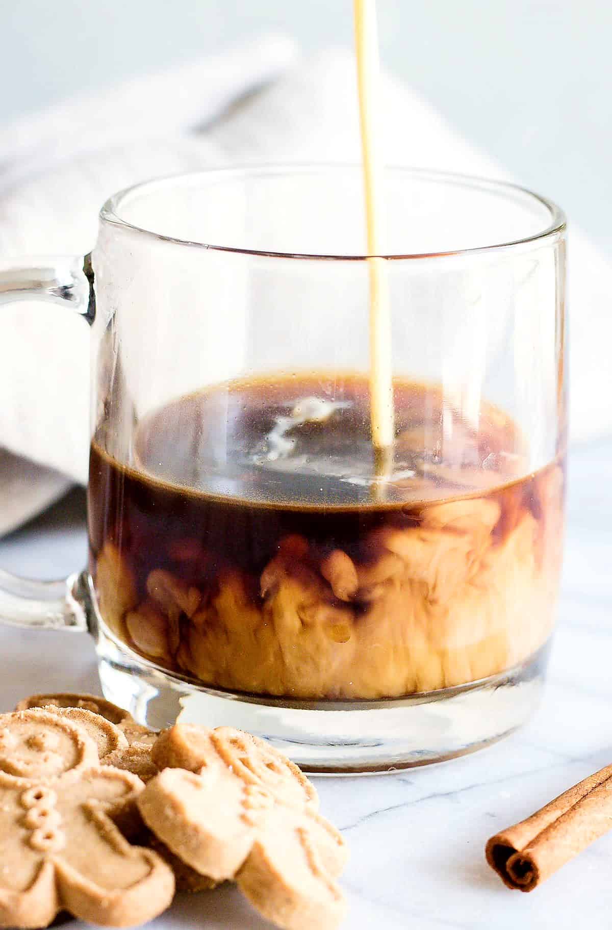 Glass mug with dark coffee and warm eggnog being poured in. 