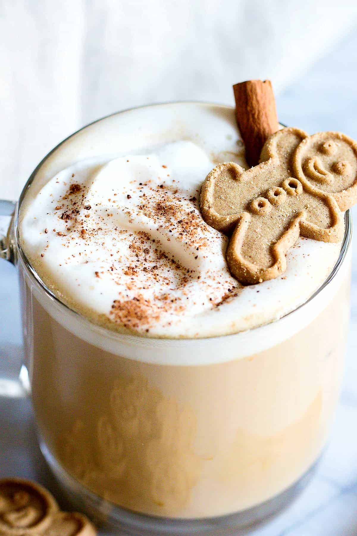 Glass mug filled with a homemade eggnog latte, topped with a gingerbread cookie and a sprinkle of nutmeg.