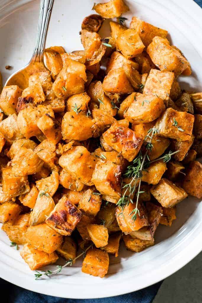 A white dish piled up with crisp roasted sweet potatoes, topped with fresh herbs. 