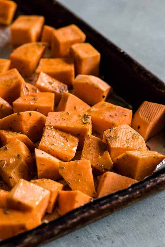 Peeled and chopped sweet potatoes ready to be roasted, coated with olive oil and sprinkled with sea salt and herbs. 