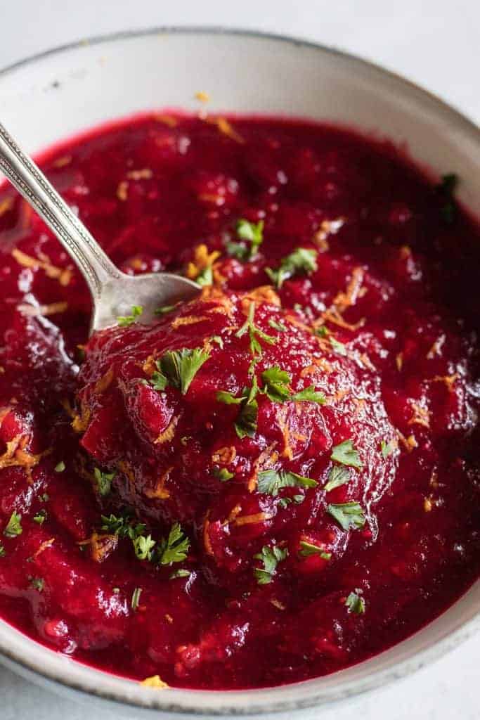 Spoon scooping up fresh homemade cranberry sauce topped with bits of parsley and orange zest.