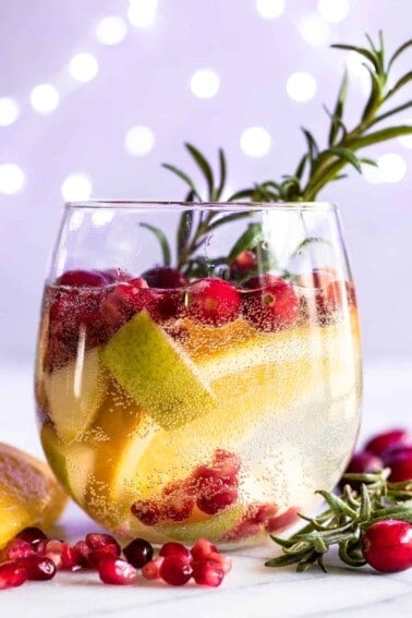 Glass filled with a Christmas white sangria garnished with rosemary.