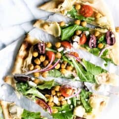 Close up of sliced flatbread pizza layered with hummus and toppings.