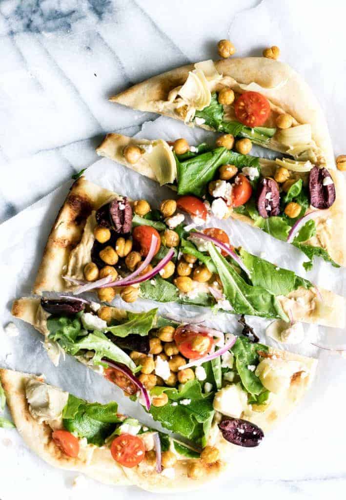 Close up of sliced flatbread pizza layered with hummus and toppings. 