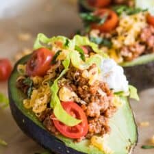 Close up of halved avocado stuffed with taco meat, cheese, lettuce, tomato and sour cream.