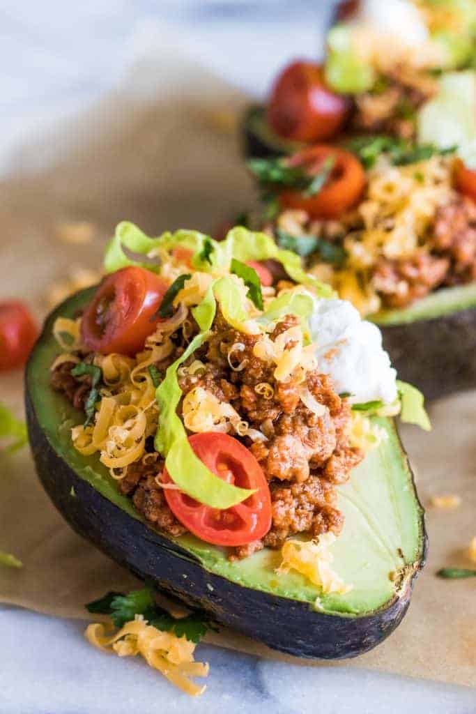 Close up of halved avocado stuffed with taco meat, cheese, lettuce, tomato and sour cream.