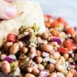 A close up of a tortilla chip dipping into Texas caviar. Black eyed peas, red onion, red bell pepper and green chiles all covered in a vinaigrette.
