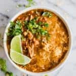 A bowl filled with chicken enchilada soup topped with cheese, cilantro and lime.