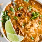 A close up of chicken enchilada soup showing cheese, cilantro, beans, chunks of chicken and tomato.