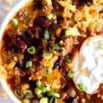 Close up image of chili topped with cheese, green onion and sour cream