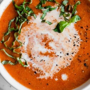 Bowl with roasted red pepper soup topped with a swirl of cream and fresh basil.