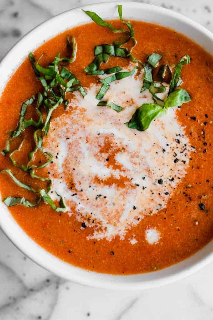 Bowl with roasted red pepper soup topped with a swirl of cream and fresh basil.