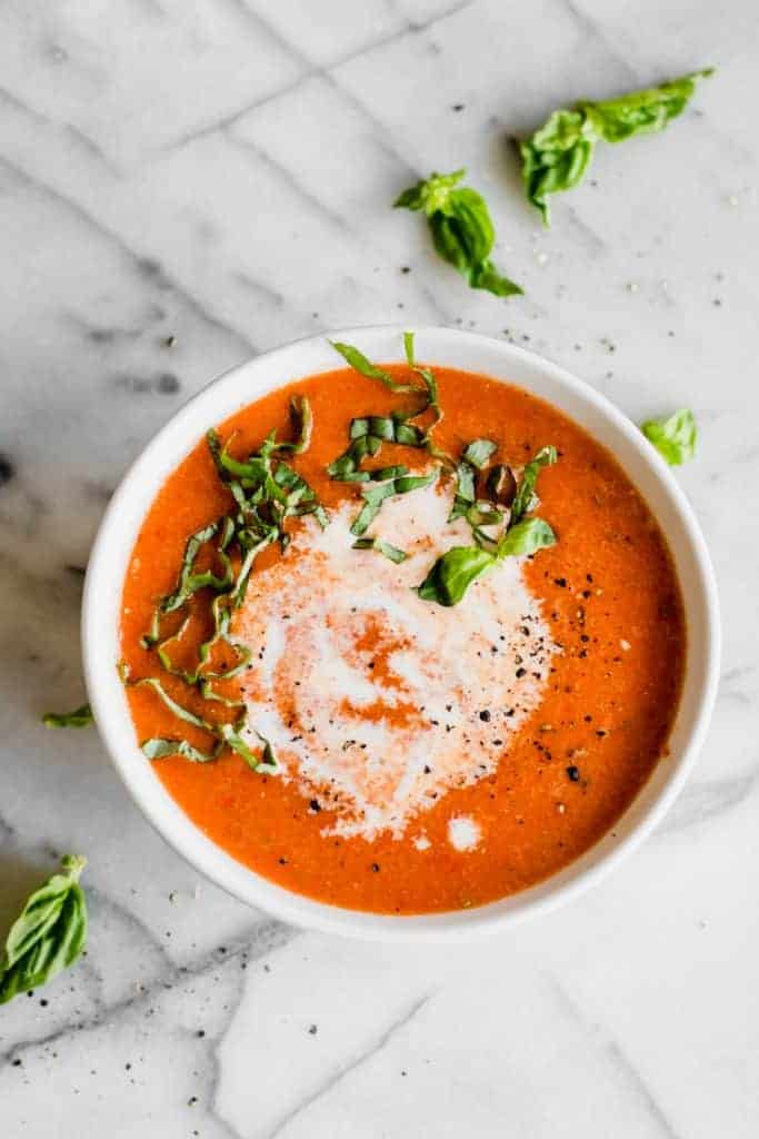 Bowl of roasted red pepper soup topped with fresh basil.