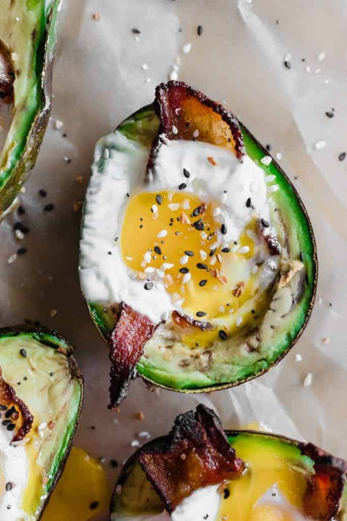 Top view of avocado crater filled with baked egg and strip of bacon.