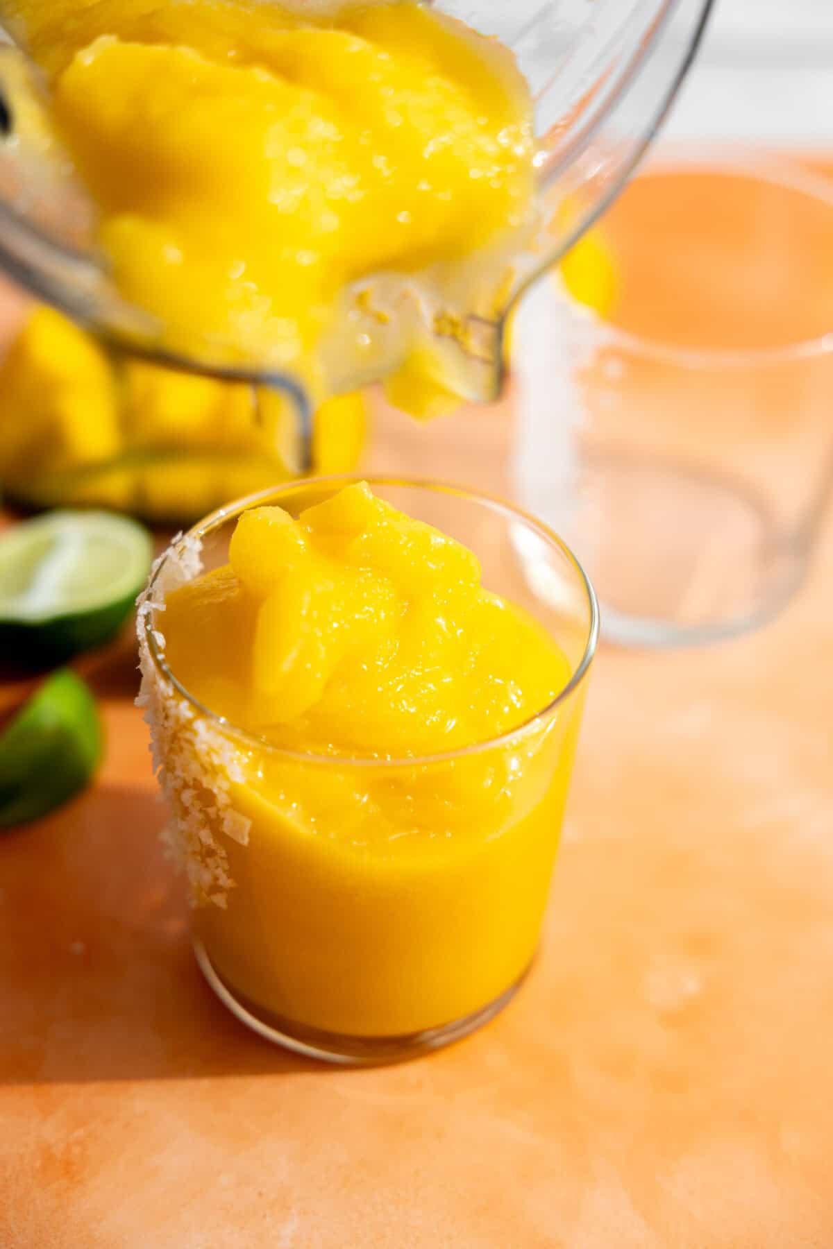 Pouring frozen mango margarita into a prepared glass with salt.