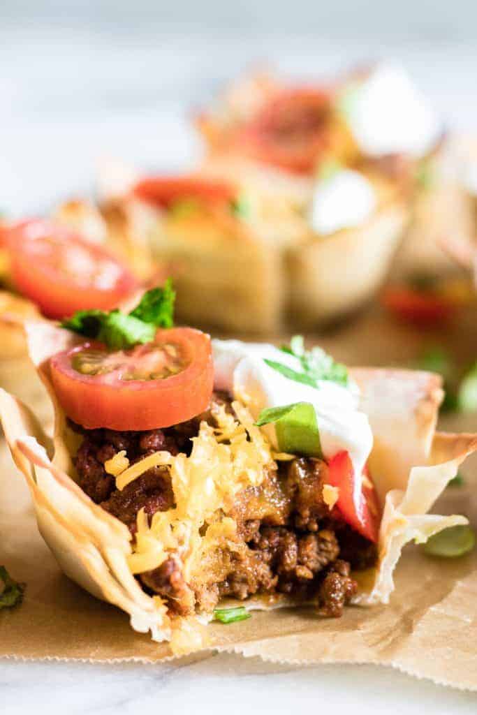 Bit into Taco Cup showing juicy taco meat, melty cheese, shredded lettuce, tomato and sprinkled cilantro.