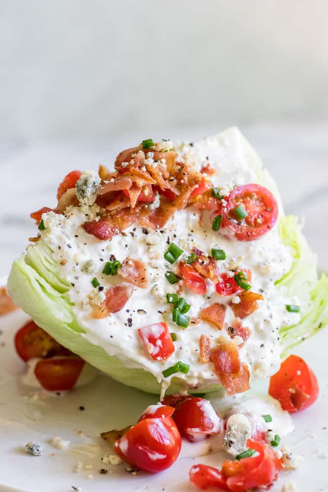Wedge salad topped with blue cheese dressing, bacon, diced tomato, chives, additional blue cheese crumbles, and cracked pepper.