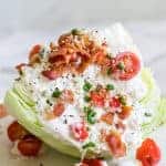 An iceberg salad dressed as a classic salad wedge with blue cheese dressing, bacon, tomato, and chives.