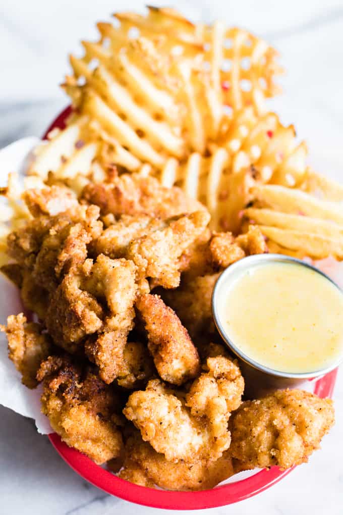 Overhead view of basket filled with waffle fries, copycat chick fil a nuggets and sauce.