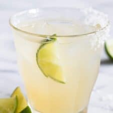 Glass full of classic margarita on ice with a lime and a salt rim.