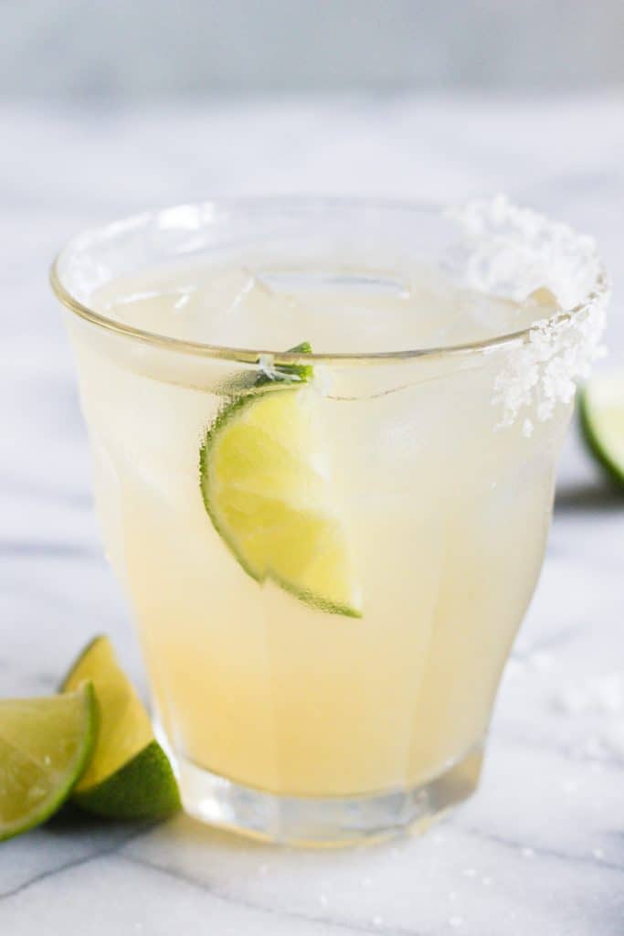 Glass full of classic margarita on ice with a lime and a salt rim. 