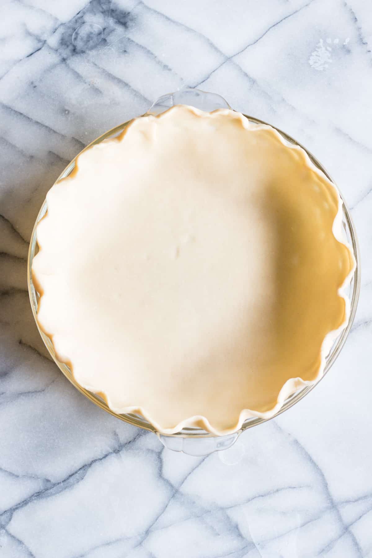 An uncooked pie crust in a glass pie dish. First steps to make a quiche.