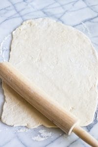 Rolling pin rolling out no yeast pizza dough.