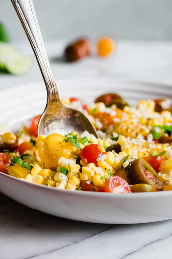 A large spoon dishing up some roasted corn salad.