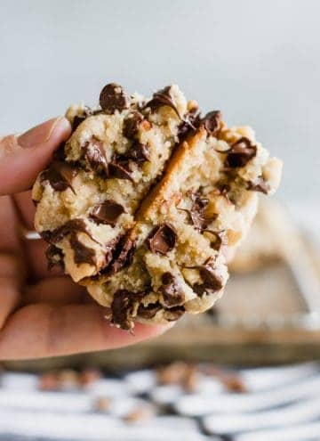 A hand holding a split open thick chocolate chip cookie with melted chocolate chips.