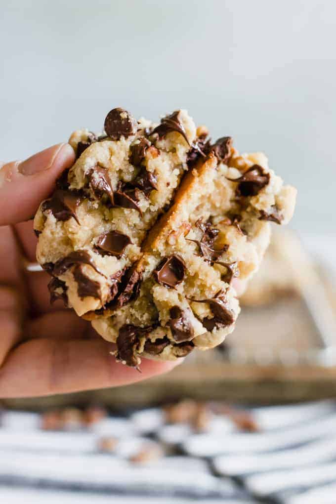 A hand holding a split open thick chocolate chip cookie with melted chocolate chips.