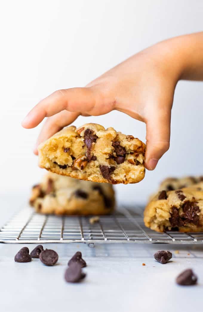 Super thick chocolate chip cookie being picked up by a hand off a cooling wire rack.