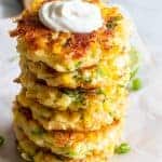 Stack of cheesy corn fritters topped with sour cream.