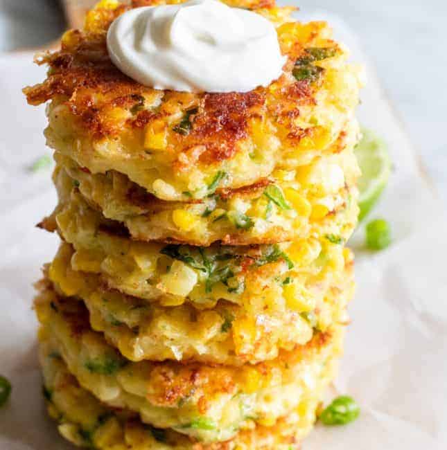 Stack of cheesy corn fritters topped with sour cream.