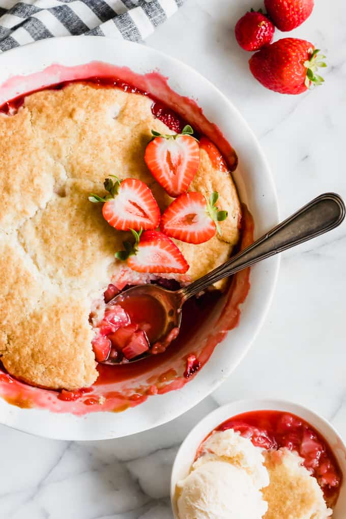 Strawberry cobbler in a dish and a bowl filled with strawberry cobbler topped with ice cream.