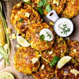 Overhead view of corn fritters with jalapeno served with sour cream and lime wedges.