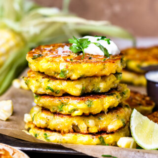 Stack of cheesy corn fritters topped with sour cream and cilantro.