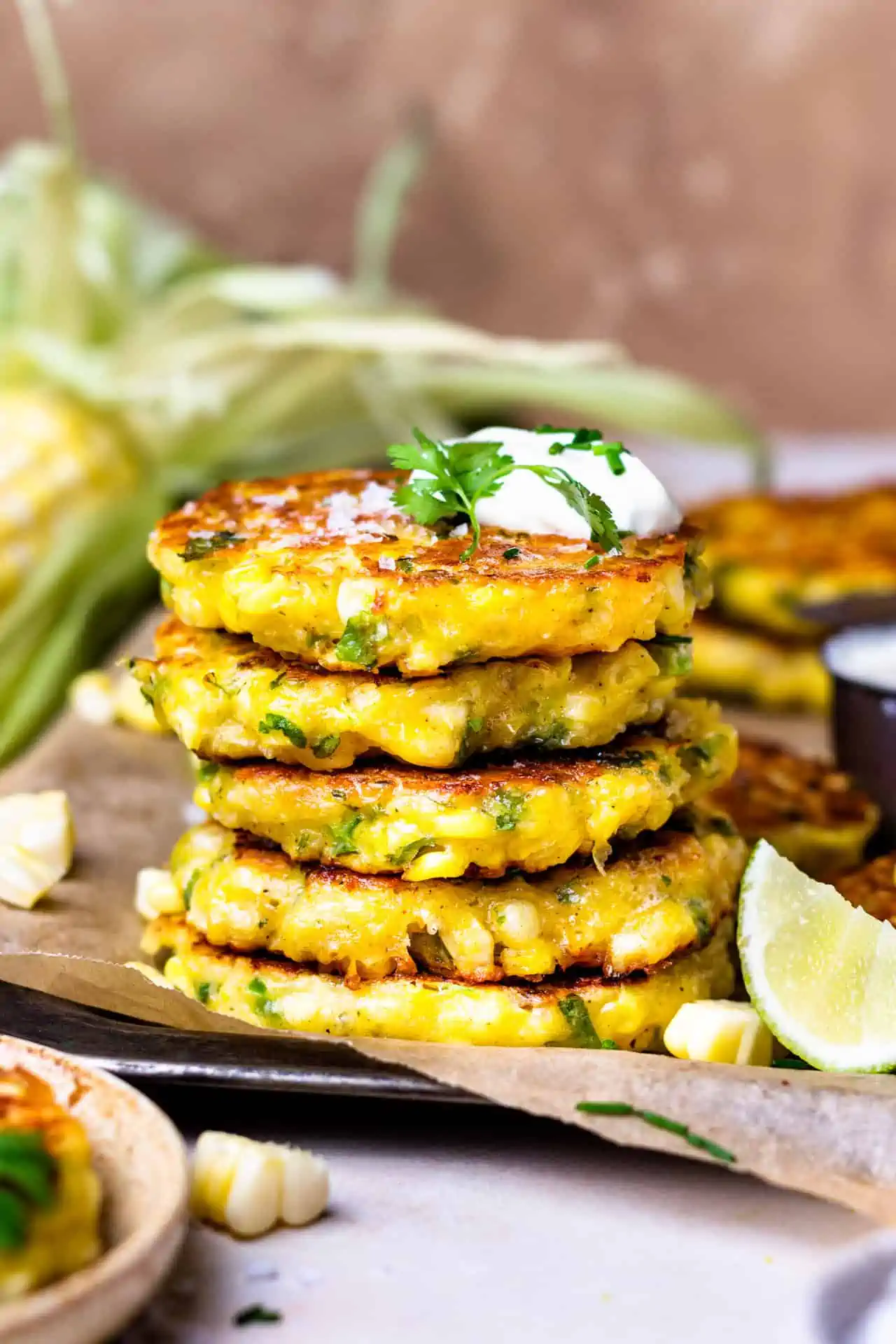 Stack of cheesy corn fritters topped with sour cream and cilantro.