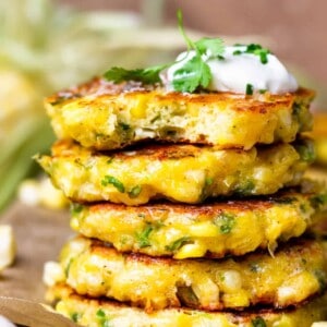 Up close view of stacked corn fritters topped with sour cream and showing the texture inside the center of a cut fritter.